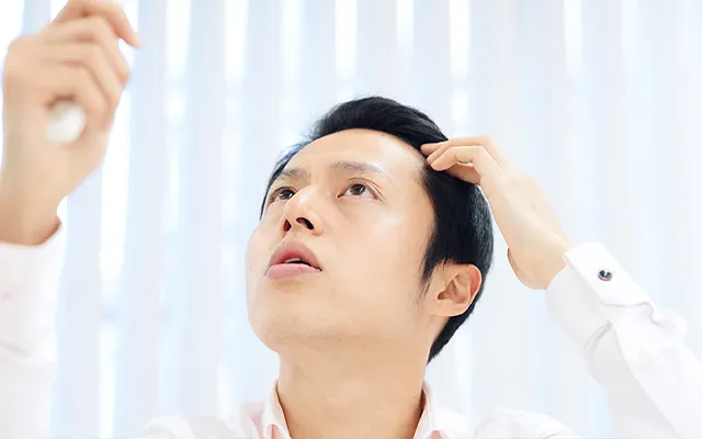 鏡で生え際を見る男性